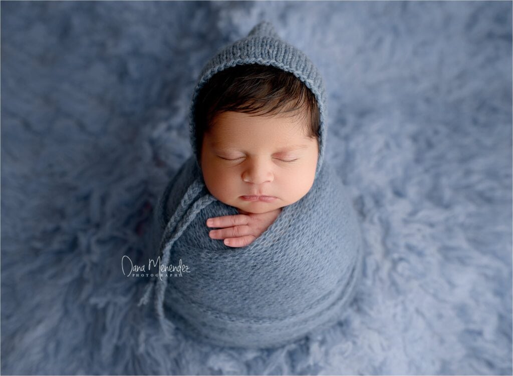 Newborn baby wrapped in blue blanket with cozy hat.