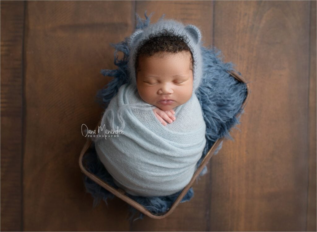 Baby wrapped in blue blanket with a matching hood, peacefully sleeping in a basket.