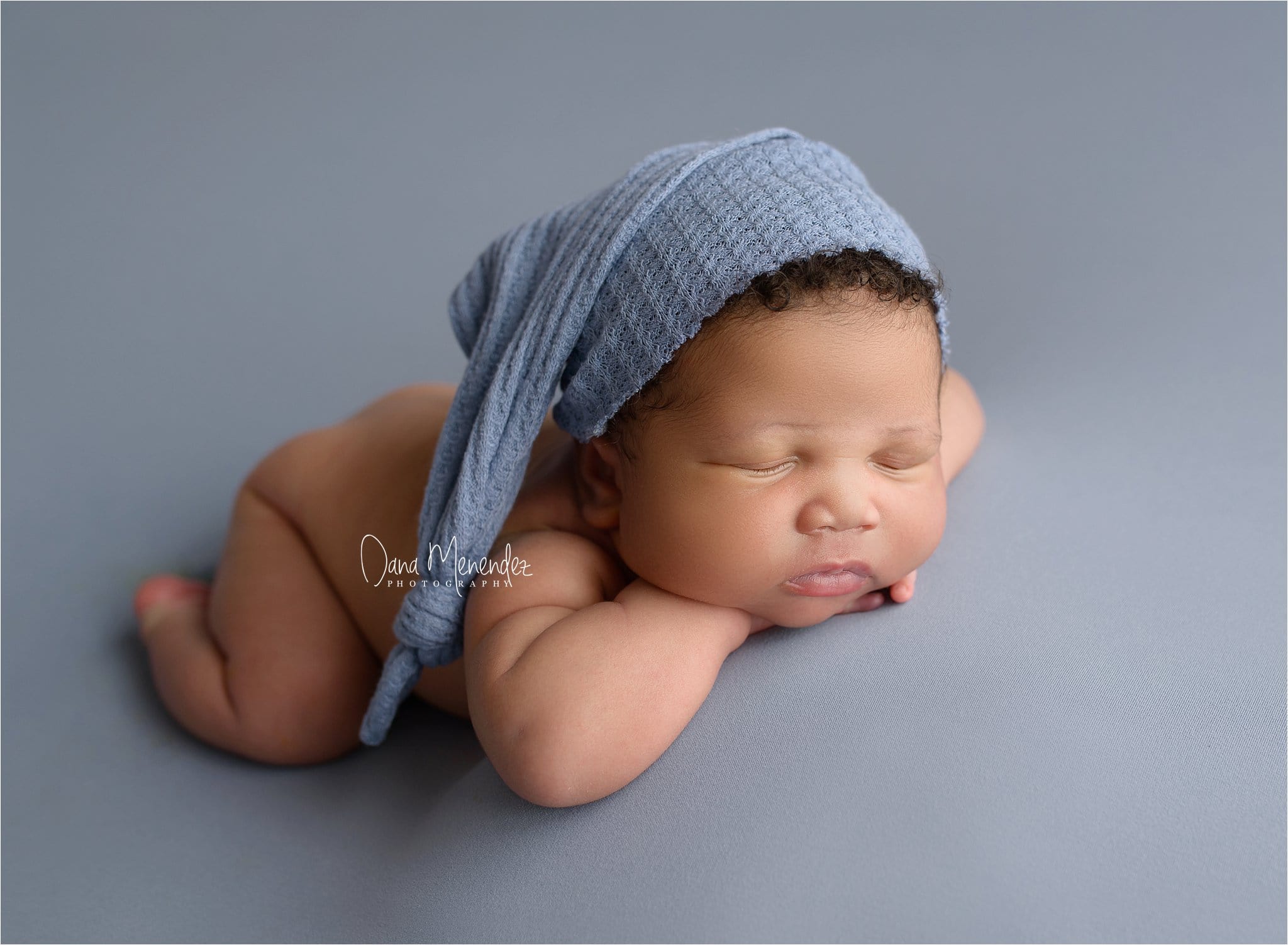 Adorable newborn baby sleeping on gray surface with a blue hat.