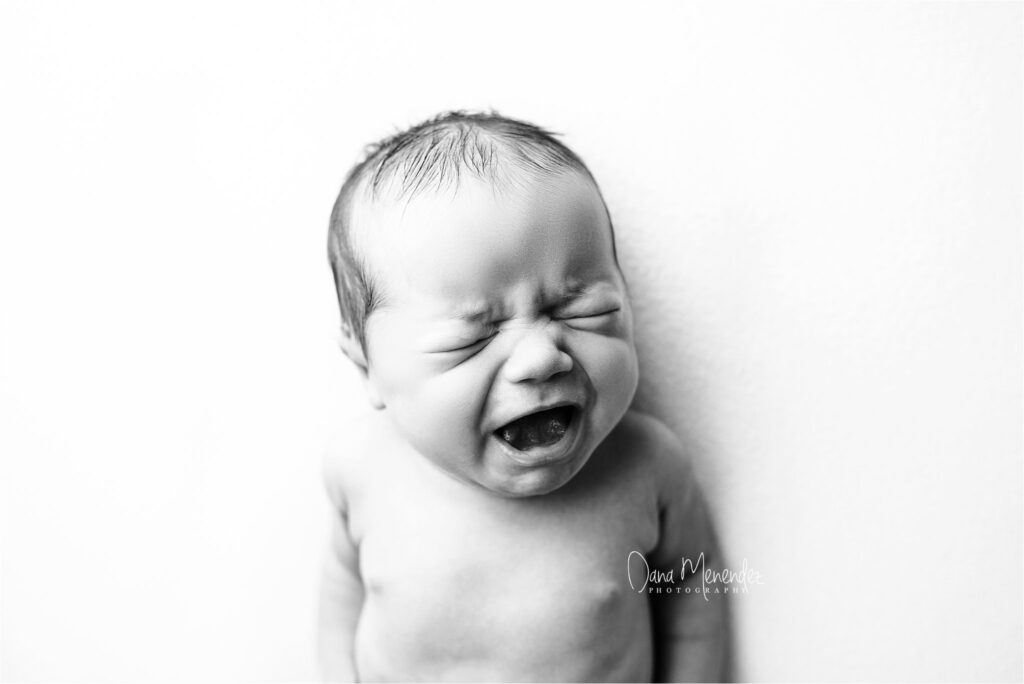 Newborn baby crying with a distressed expression, captured in black and white.