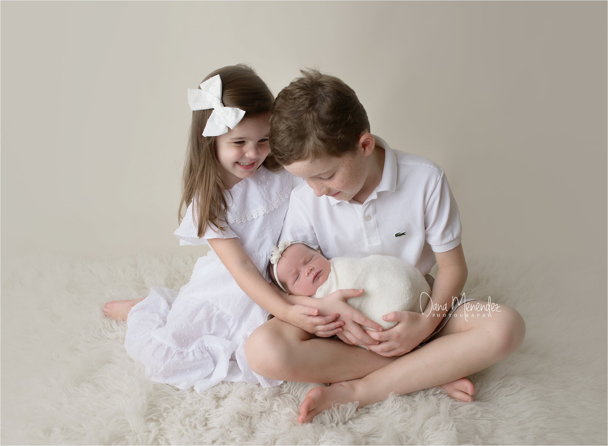 Adorable siblings with newborn baby in a studio setting.