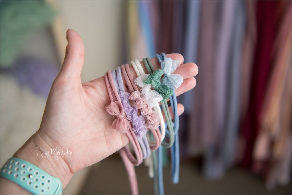 Baby headbands with pastel bows and ribbons held in a person's hand.