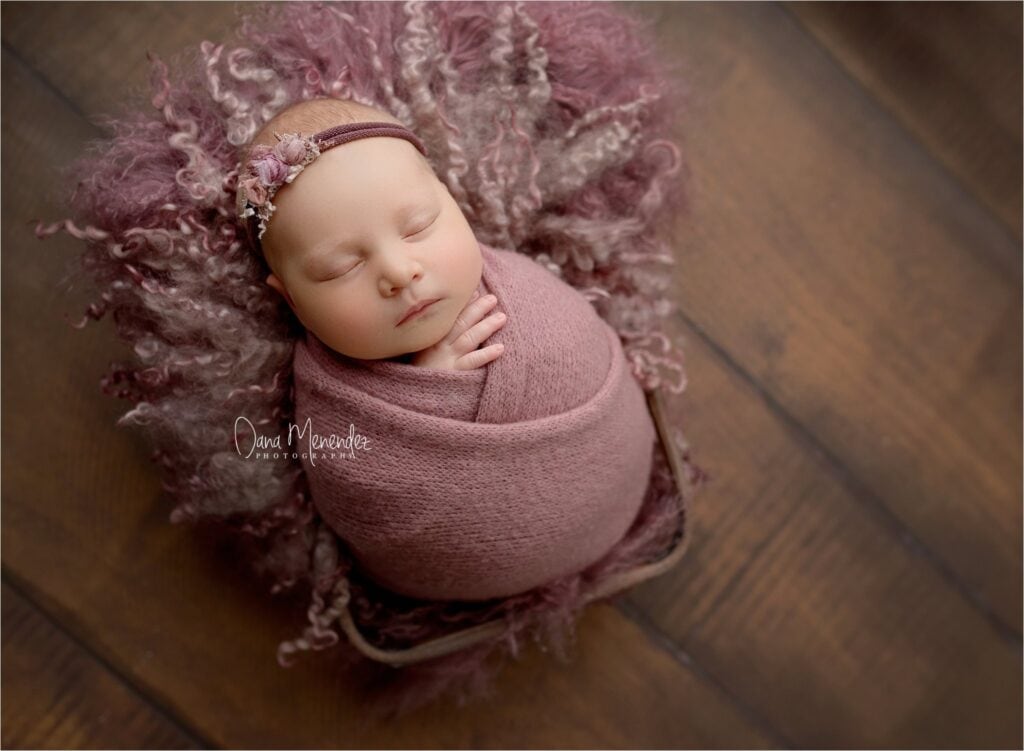 Baby girl sleeping peacefully wrapped in pink, lying on a wooden floor.