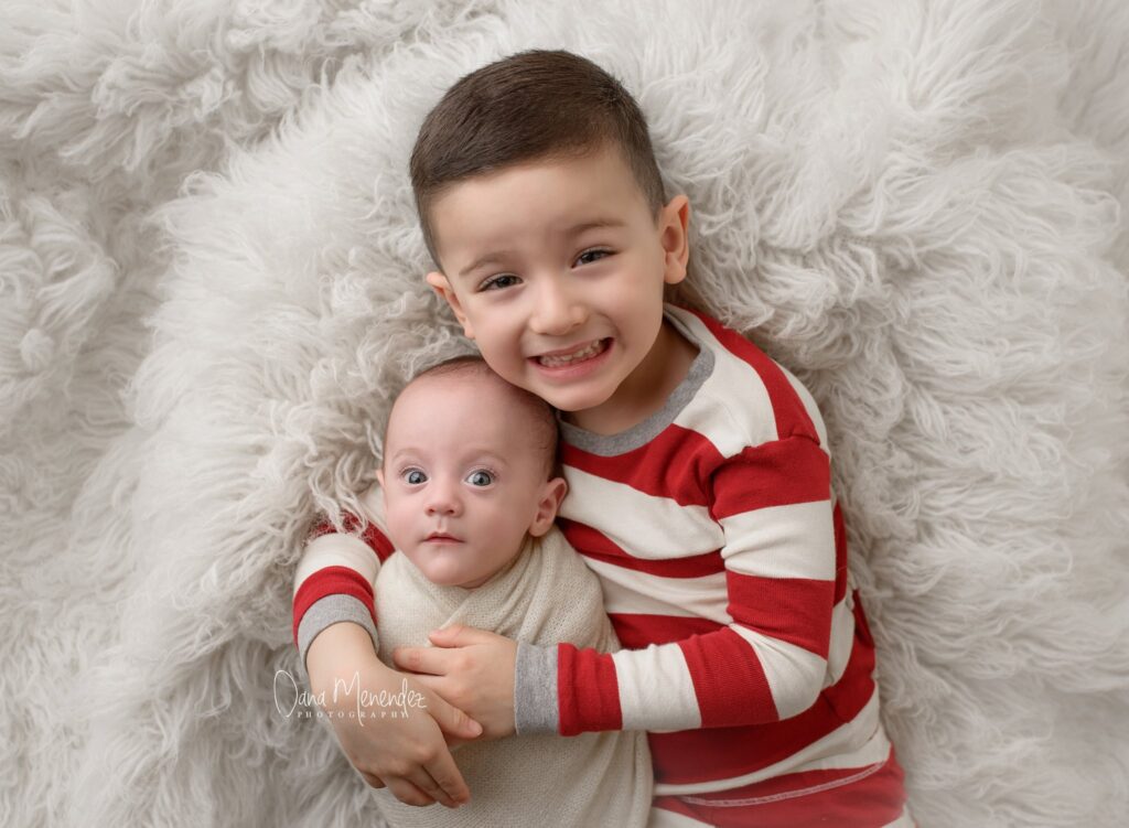 Adorable young boy and baby sibling lying together on fluffy white blanket.