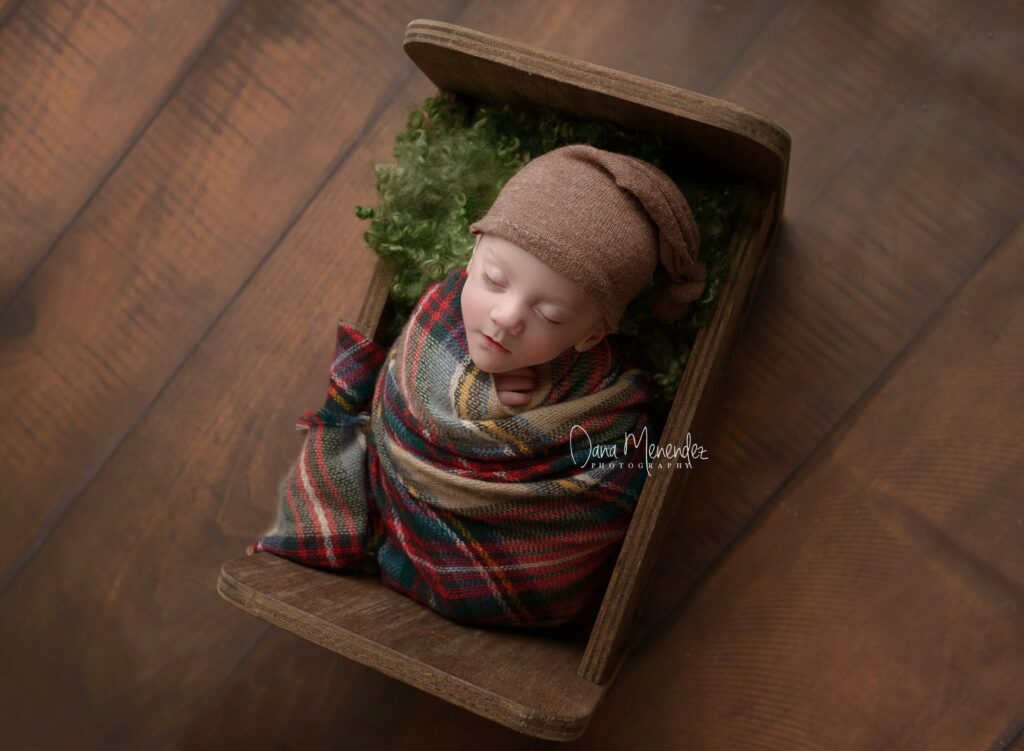 Adorable newborn baby wrapped in a plaid blanket in a wooden box.