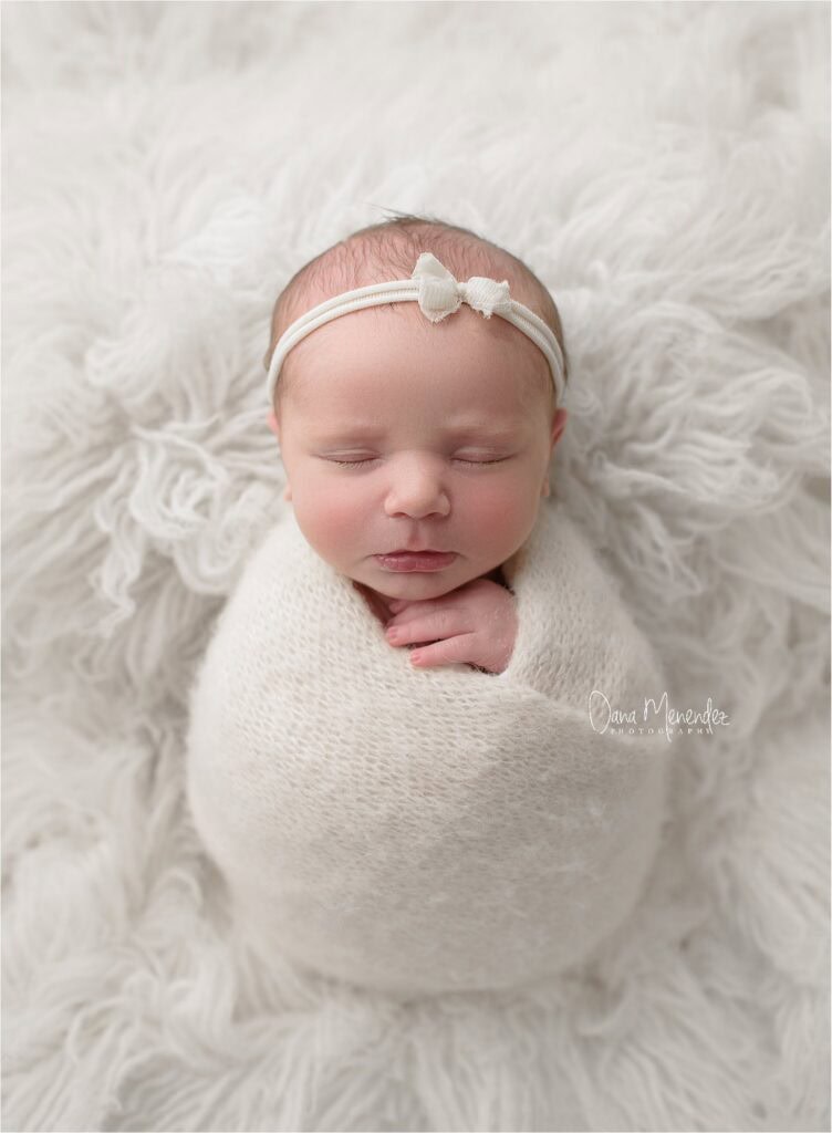 Newborn baby girl peacefully sleeping, wrapped in a soft white blanket with a delicate headband.