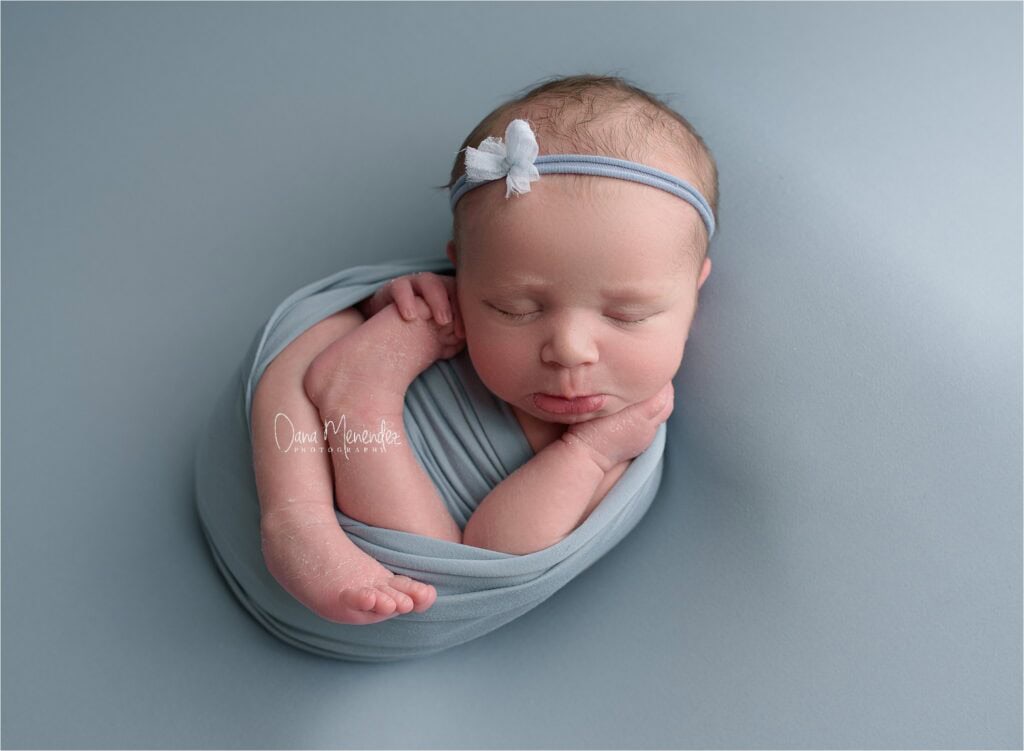 Baby girl peacefully sleeping in a blue wrap with a matching headband.