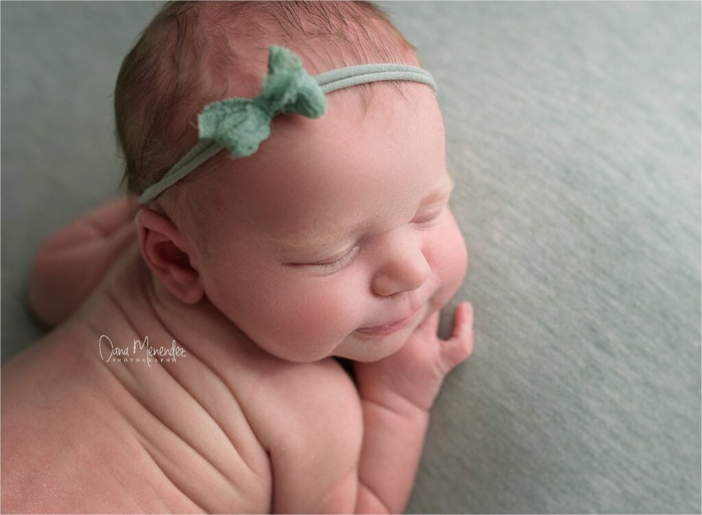 Adorable newborn girl with a green headband, peacefully sleeping on a soft textured surface.