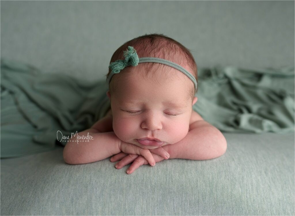 Adorable sleeping newborn girl with headband on soft green blanket.