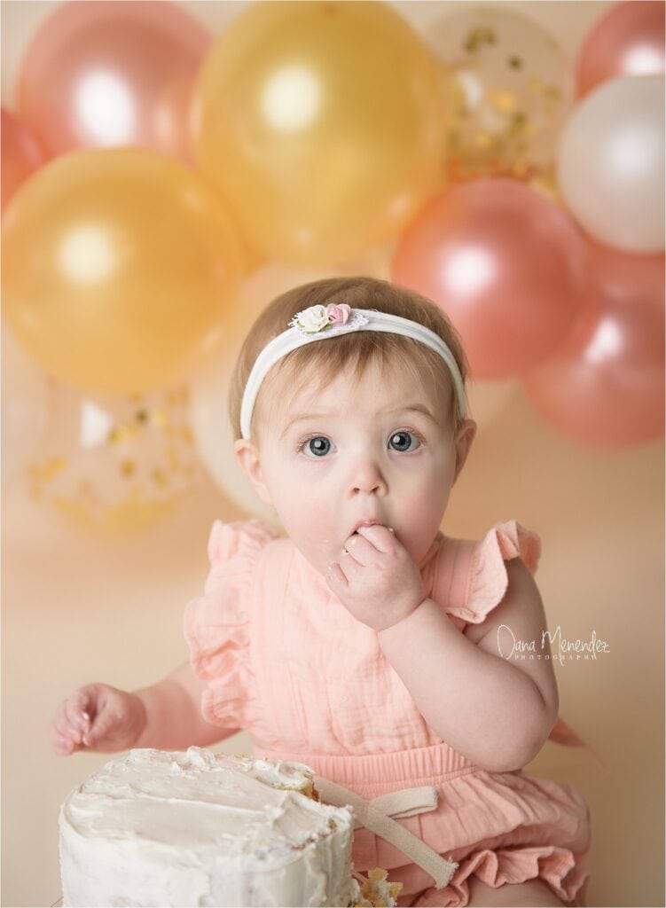Baby girl with cake and balloons for birthday celebration.