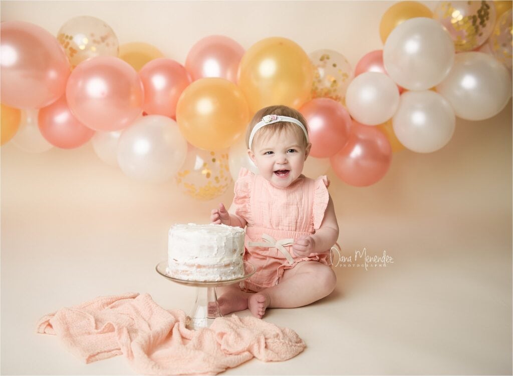 Adorable baby girl celebrating her first birthday with cake and balloons.