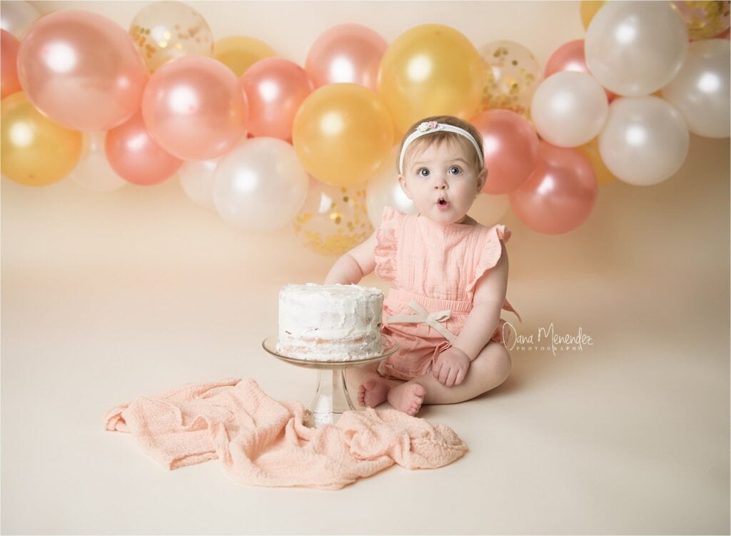 Baby girl celebrating birthday with cake and balloons.