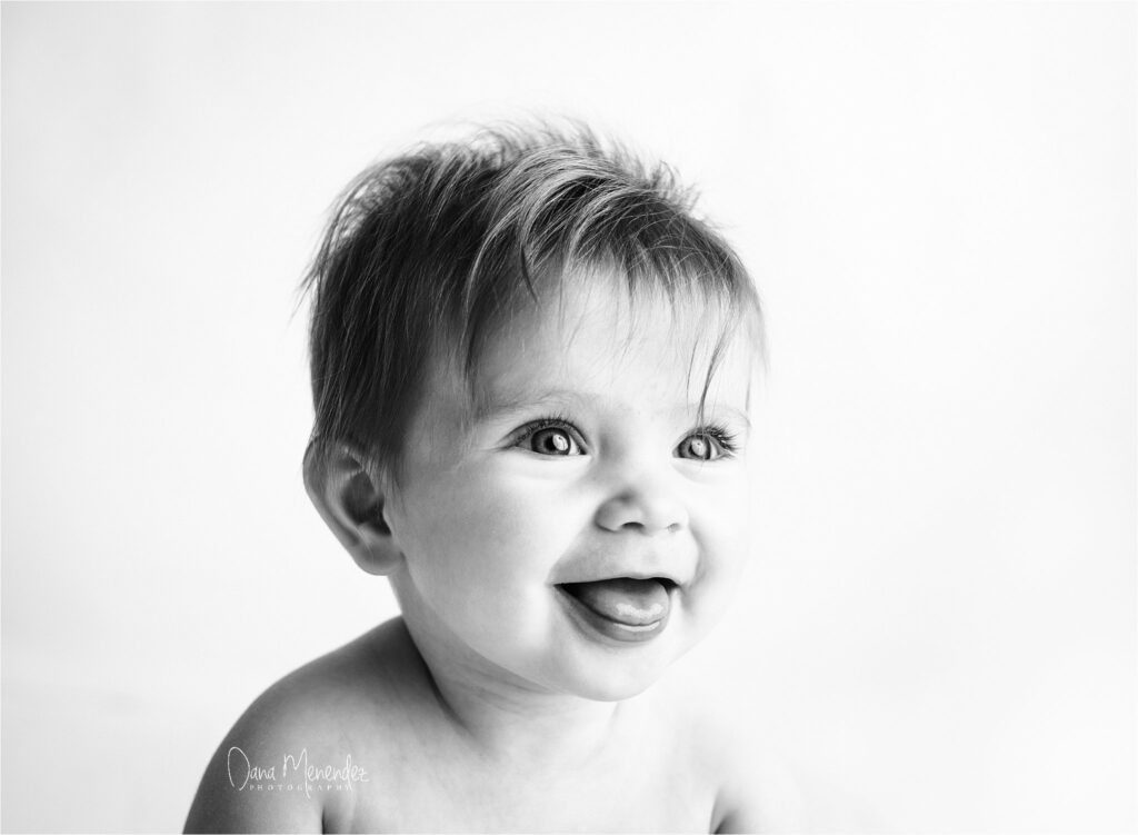 Baby smiling with open mouth and bright eyes in a black and white portrait.