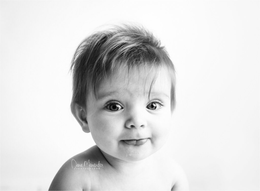 Baby's face with big eyes and playful expression in black and white.