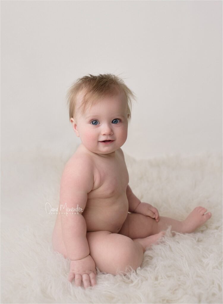Adorable newborn baby with blue eyes sitting on a fluffy white blanket, looking at the camera with a.