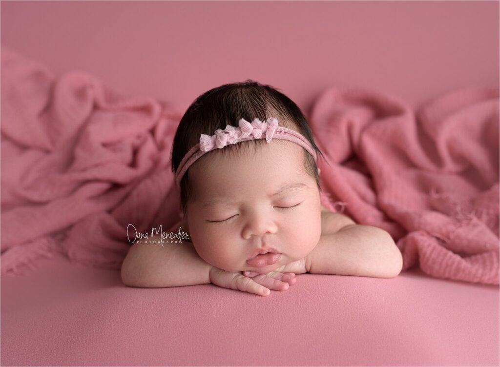 Adorable sleeping newborn girl with headband on pink blanket.
