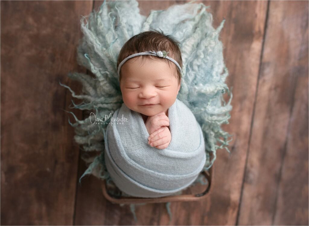 Newborn baby wrapped in a cozy blanket with a delicate headband, resting peacefully on a rustic wood.
