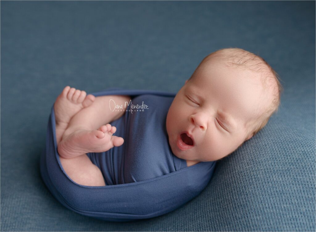 Baby sleeping peacefully in a blue wrap on a soft blue background.