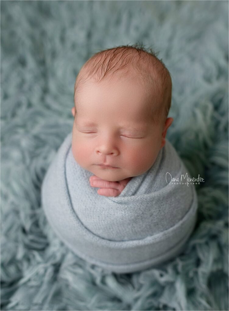 Adorable newborn baby peacefully sleeping in a gray swaddle.