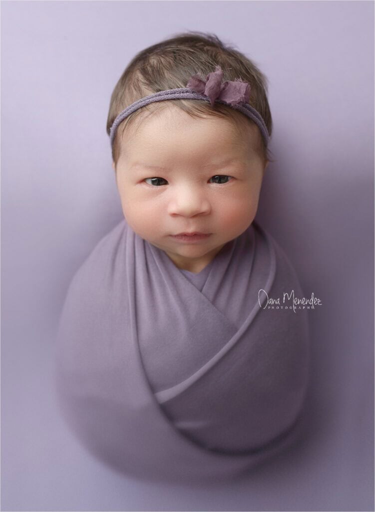 Baby girl in lavender wrap with headband, looking directly at the camera.