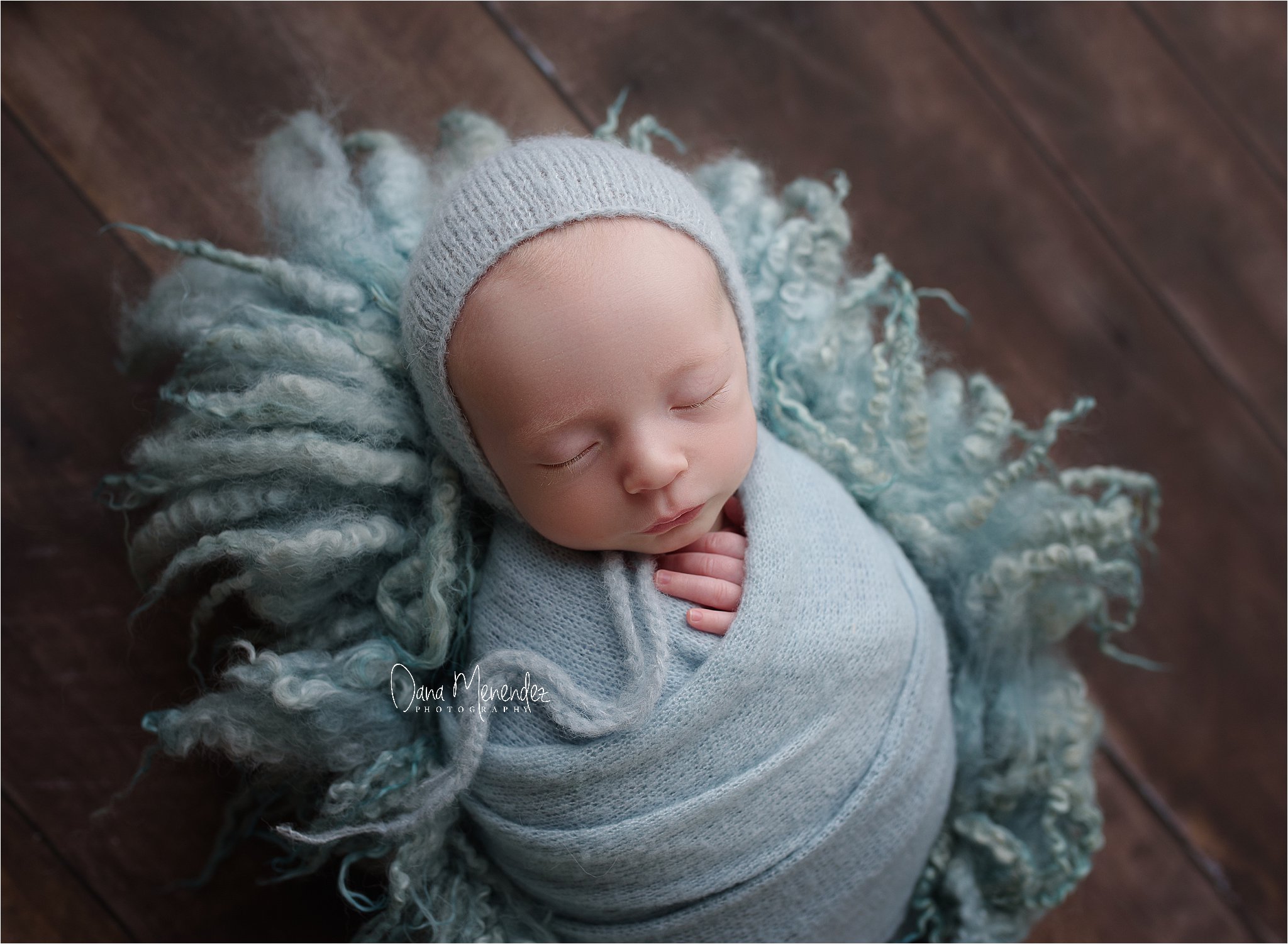 Newborn baby sleeping peacefully in cozy gray wrap and hat.