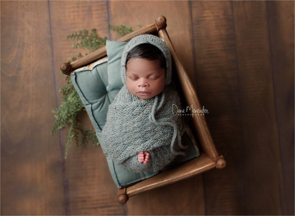 Newborn baby wrapped in cozy gray blanket, sleeping peacefully in a small wooden bed.