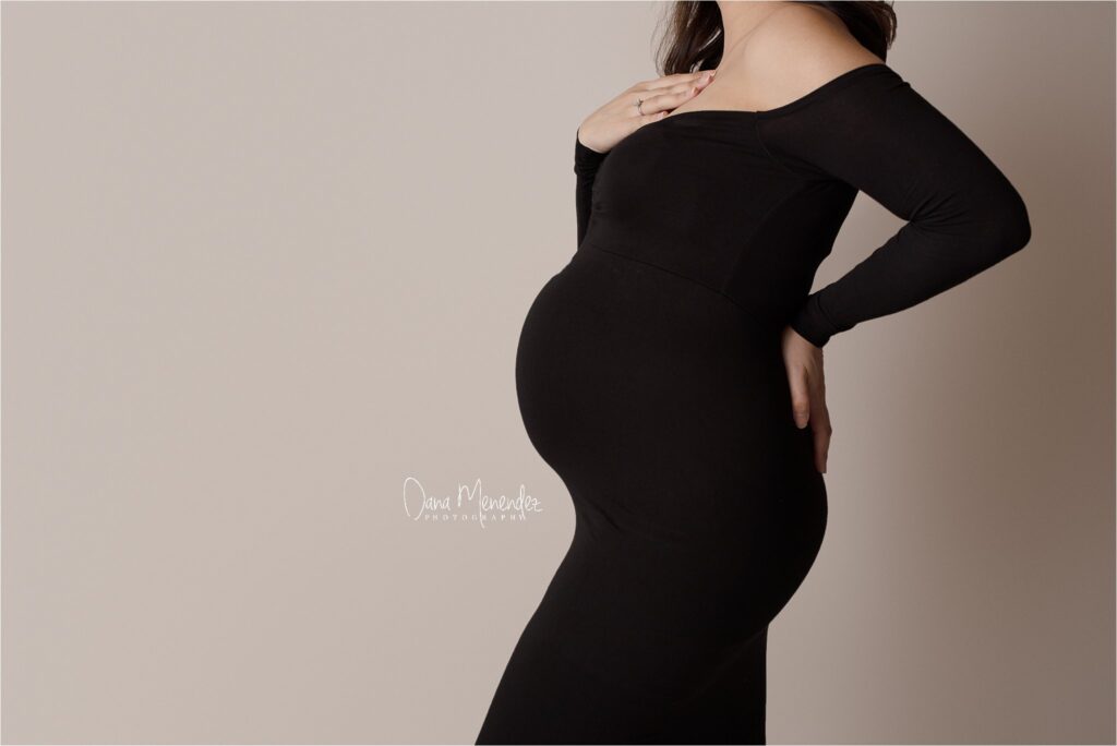 Pregnant woman in a black dress, gently holding her belly, showcasing maternity photography.