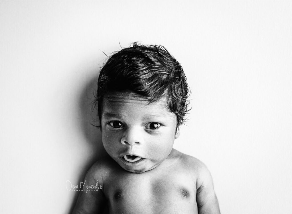 Baby portrait in black and white with expressive eyes and curly hair.