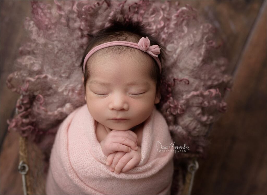 Newborn girl peacefully sleeping with pink headband and blanket in Okotoks.
