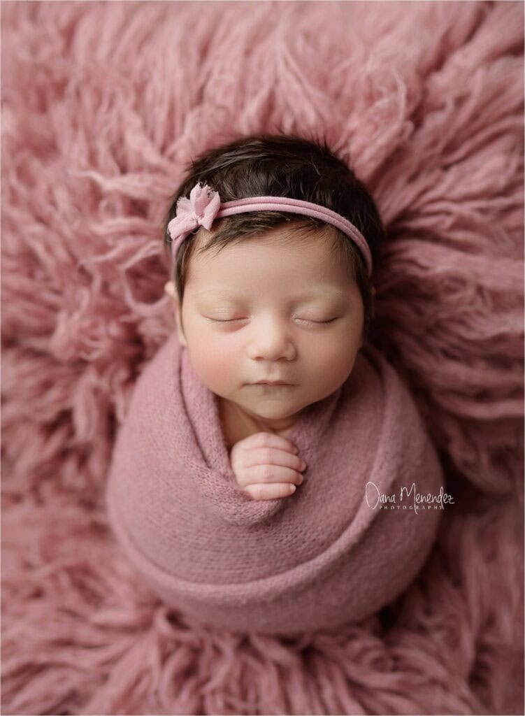 Newborn girl peacefully sleeping wrapped in pink, on soft pink blanket.