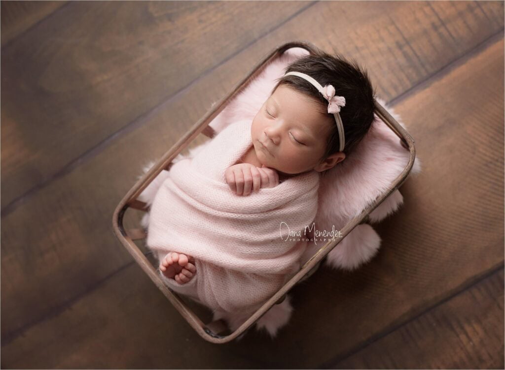 Baby girl sleeping peacefully in a pink wrap with a matching headband.