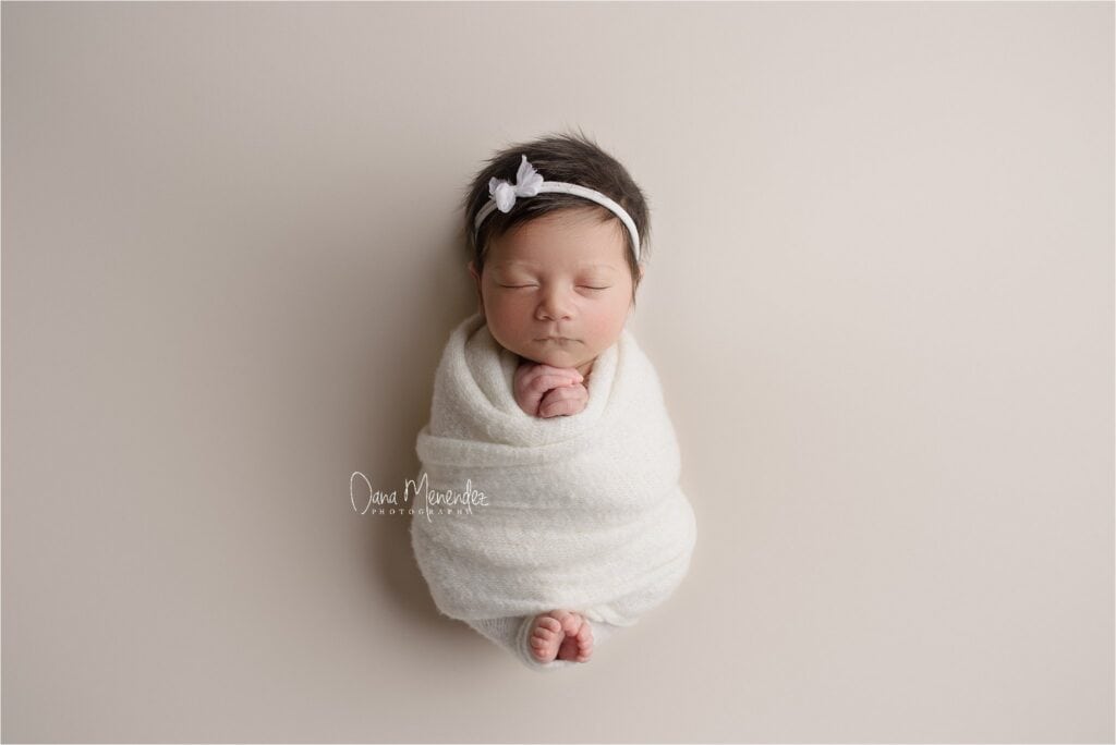 Adorable newborn baby girl wrapped in a white swaddle with a headband.