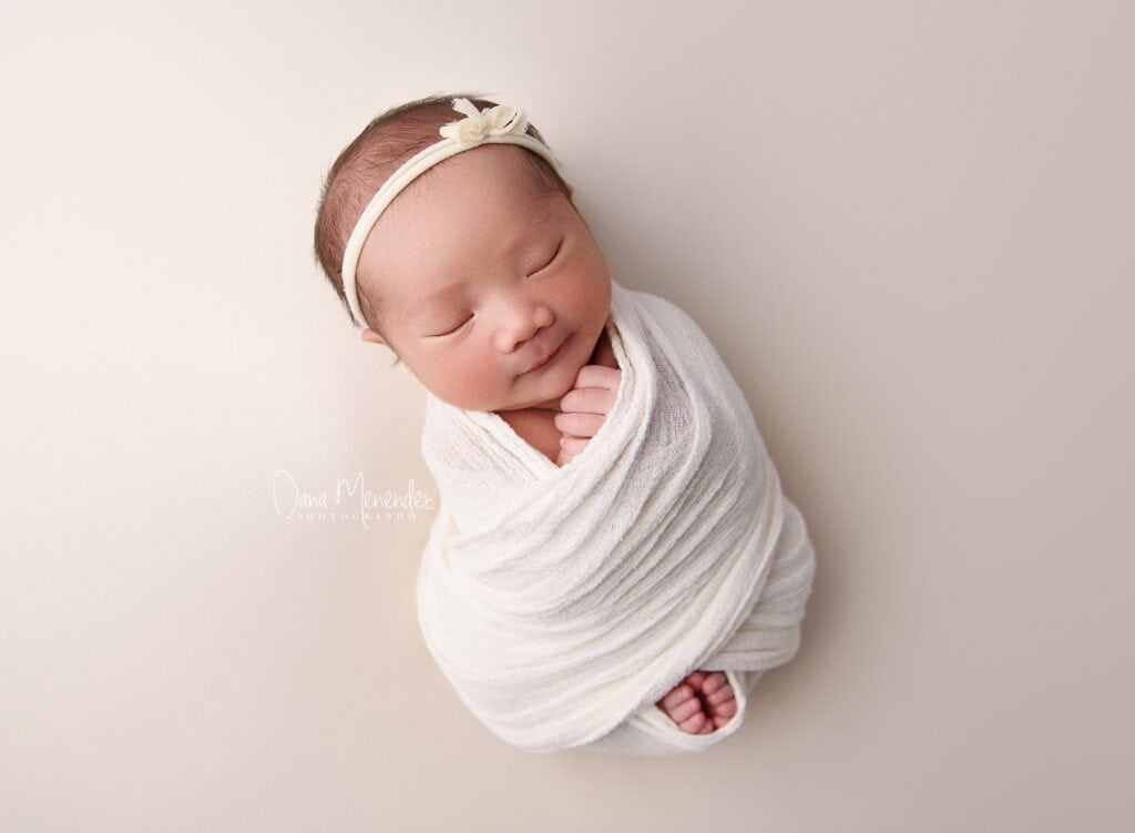 Baby sleeping peacefully wrapped in a white swaddle with a headband.