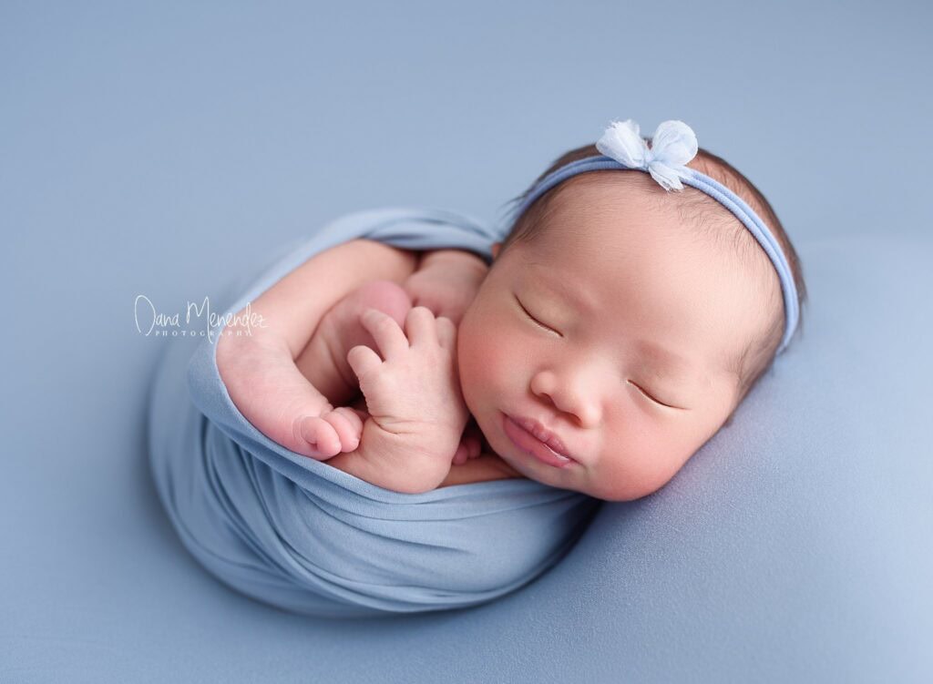 Adorable sleeping newborn baby wrapped in blue, wearing a matching headband.