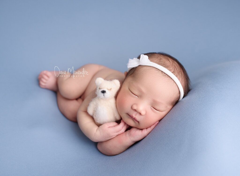 Adorable sleeping newborn baby girl with teddy bear on a soft blue blanket.
