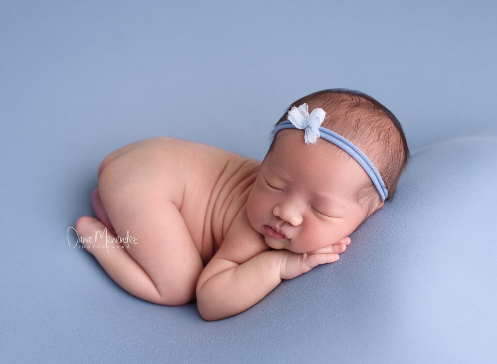 Baby girl peacefully sleeping on a soft blue surface with a matching headband.