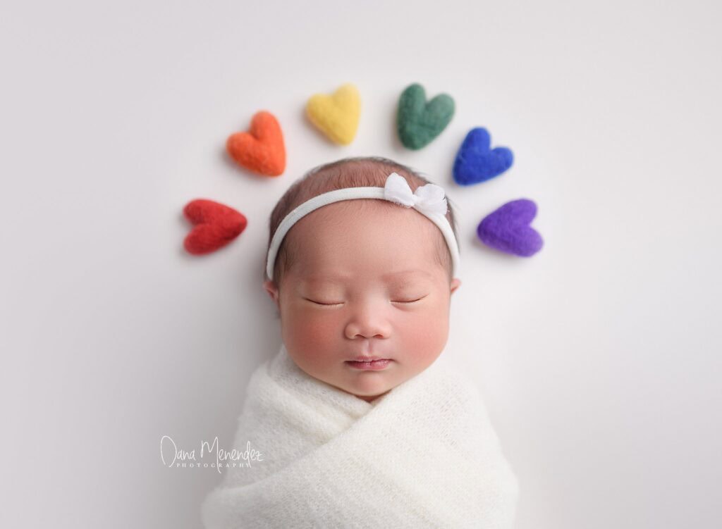 Adorable newborn baby with colorful felt hearts around head, peaceful sleep.