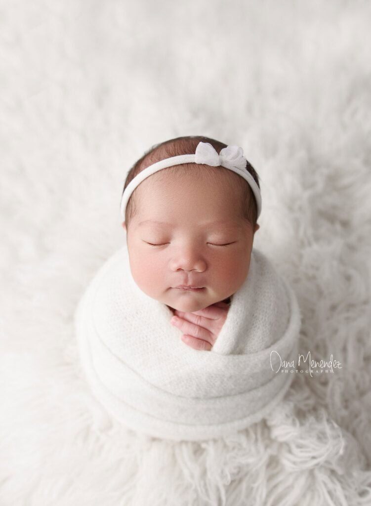 Baby girl peacefully sleeping with a white headband and wrap.