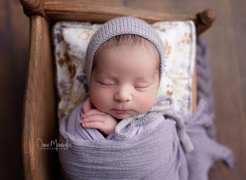 Adorable newborn baby peacefully sleeping wrapped in a gray blanket.