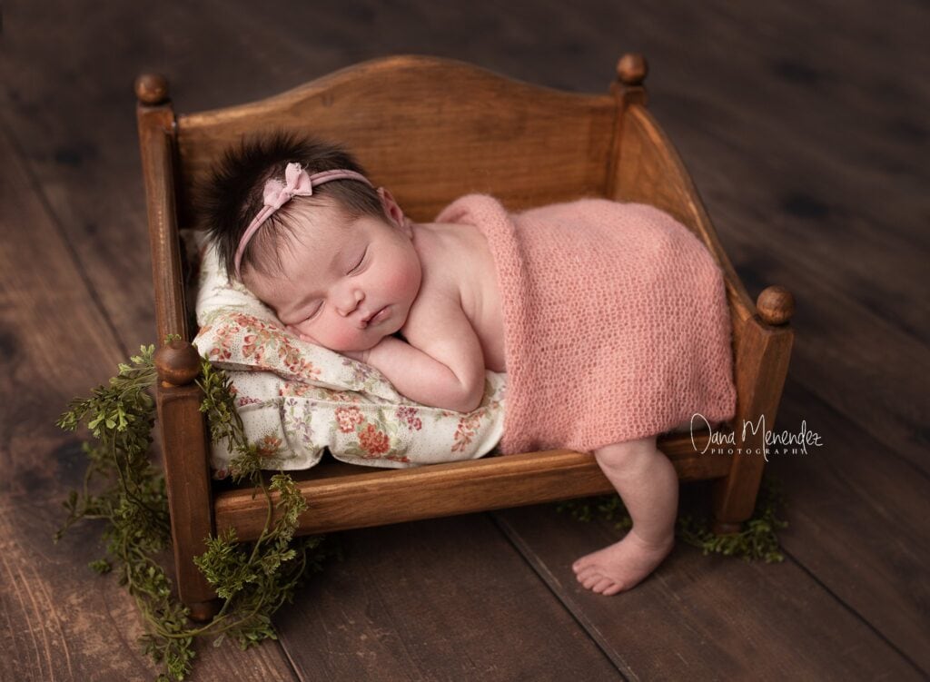 Baby sleeping peacefully in a small wooden bed with pink blanket.