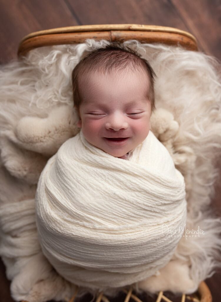Adorable newborn baby wrapped in a cream blanket, smiling peacefully.