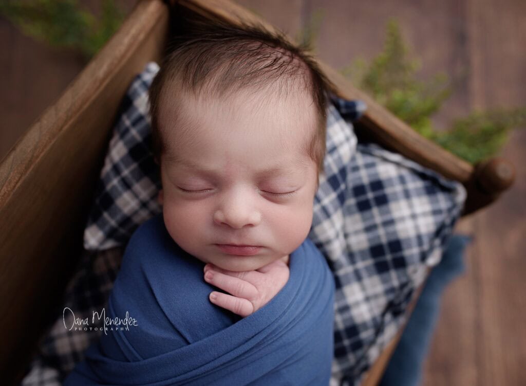 Adorable newborn sleeping peacefully in a blue wrap in a cozy setting.