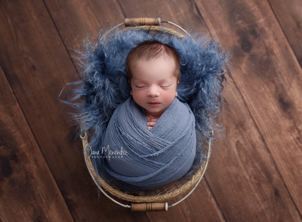 Baby wrapped in blue swaddle sleeping in a basket.