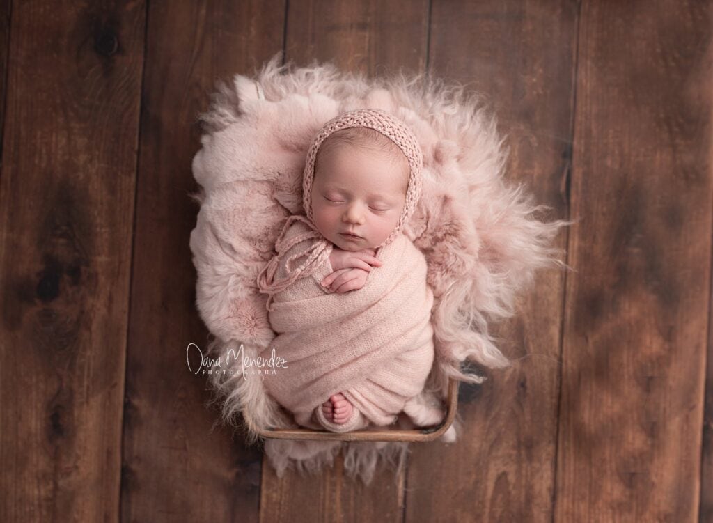 Adorable newborn girl sleeping in pink wrap on fluffy blanket.