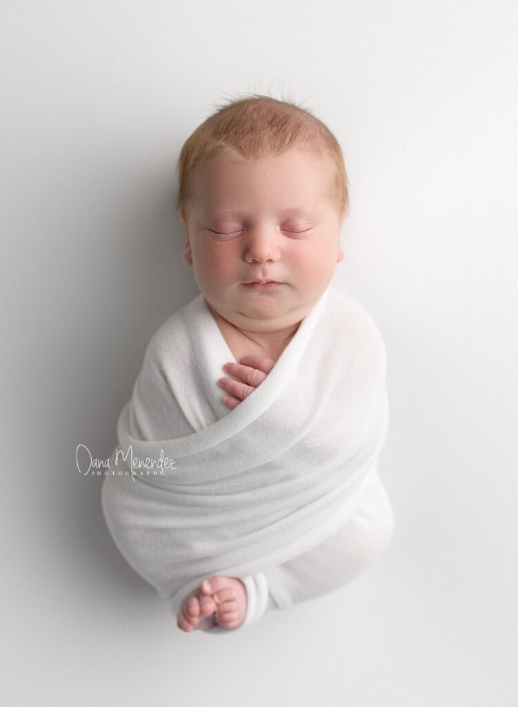 Adorable newborn baby peacefully sleeping in a white swaddle.