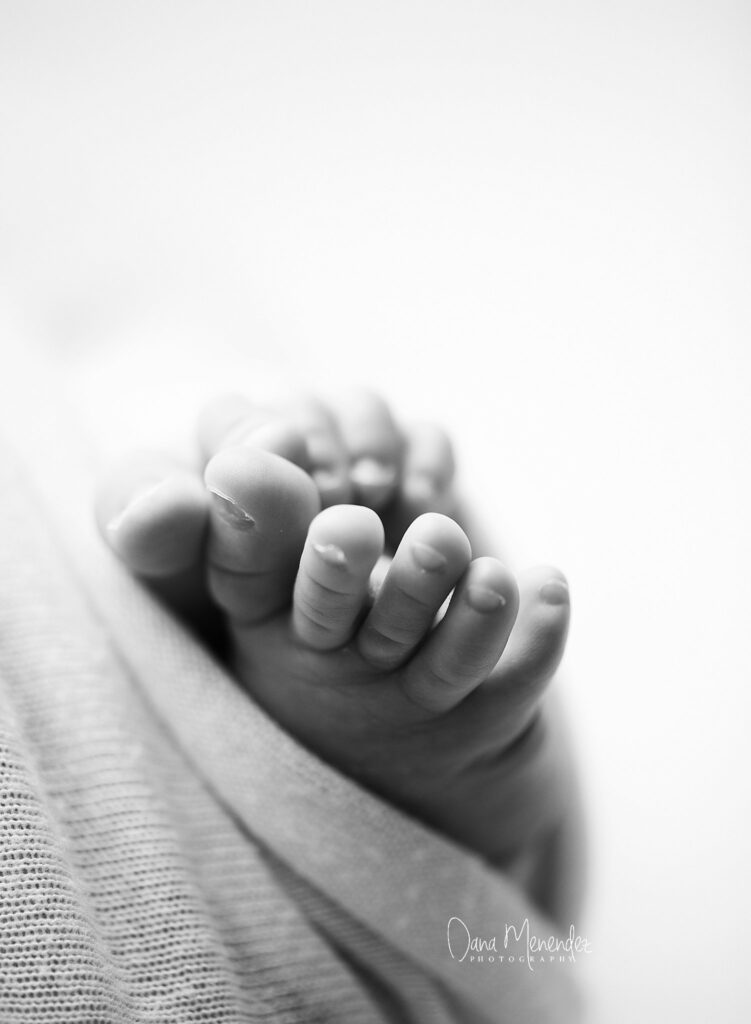 Baby's tiny hand grasping an adult finger in black and white.
