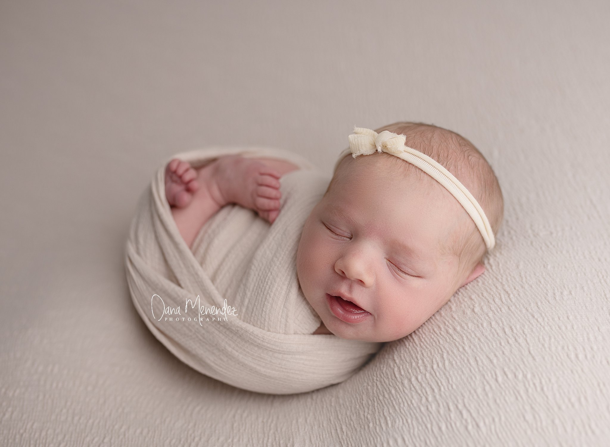 Adorable newborn baby peacefully sleeping in a cream wrap with headband.