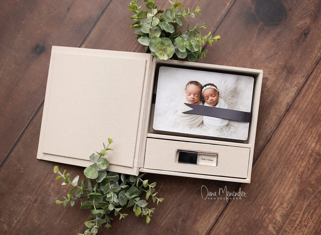 Newborn baby photo in a gift box with eucalyptus leaves on a wooden surface.