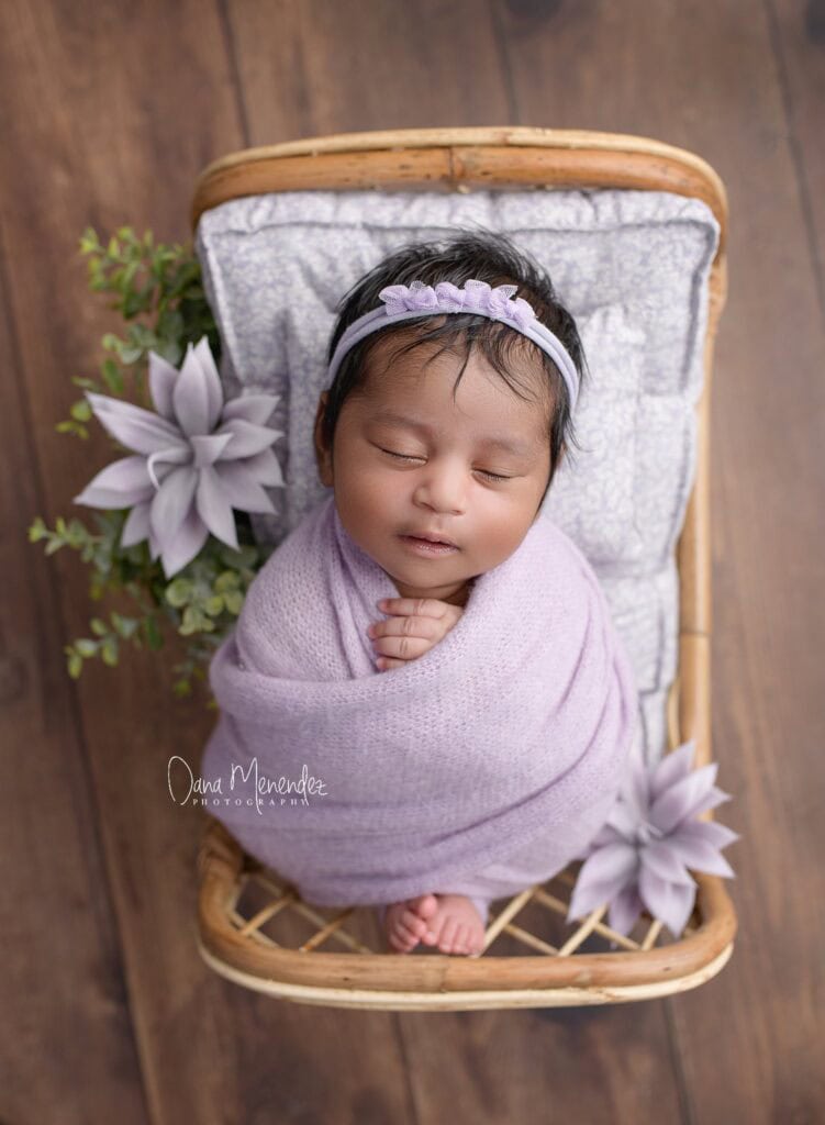 Baby girl wrapped in lavender blanket with headband.