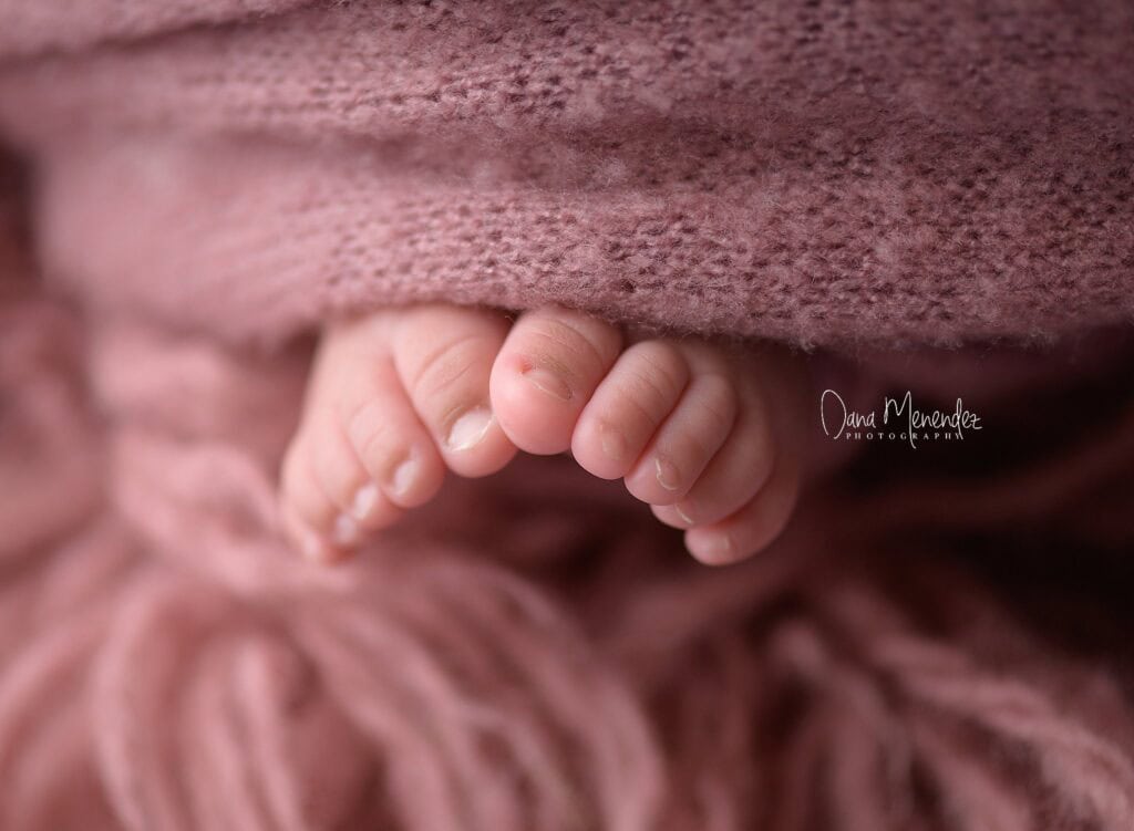 Newborn feet wrapped in soft pink fabric, showcasing delicate tiny toes.